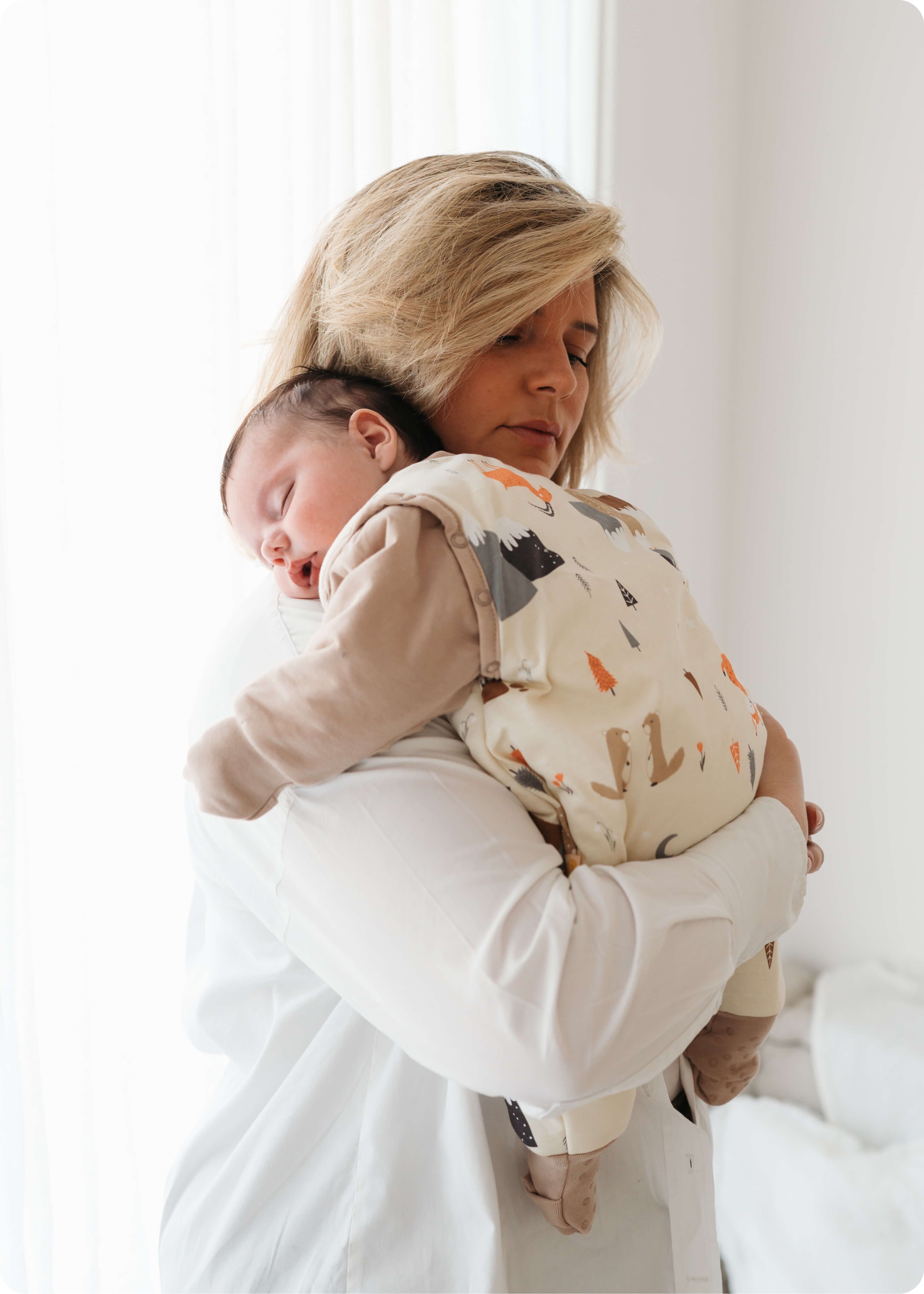 Maminka držící na rameni spící dítě ve spacím pytli